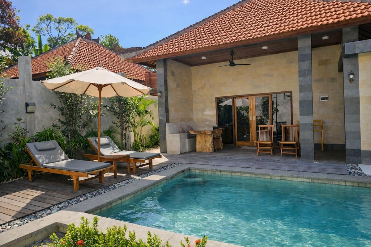 A pool area with lounge chairs, a wooden deck, and a covered patio with chairs and a table.