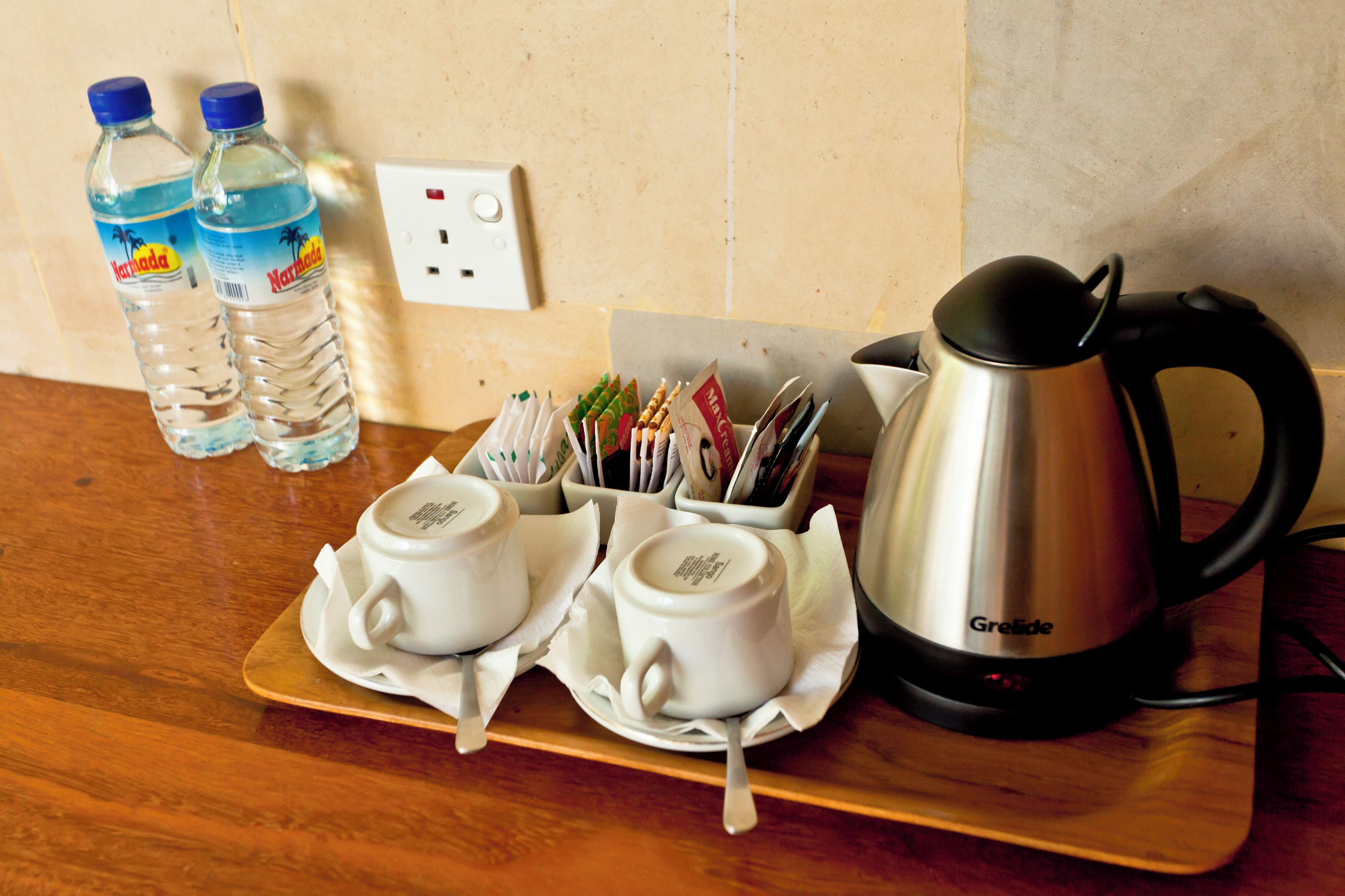 A tray with two white cups, a kettle, and two water bottles on a wooden table.