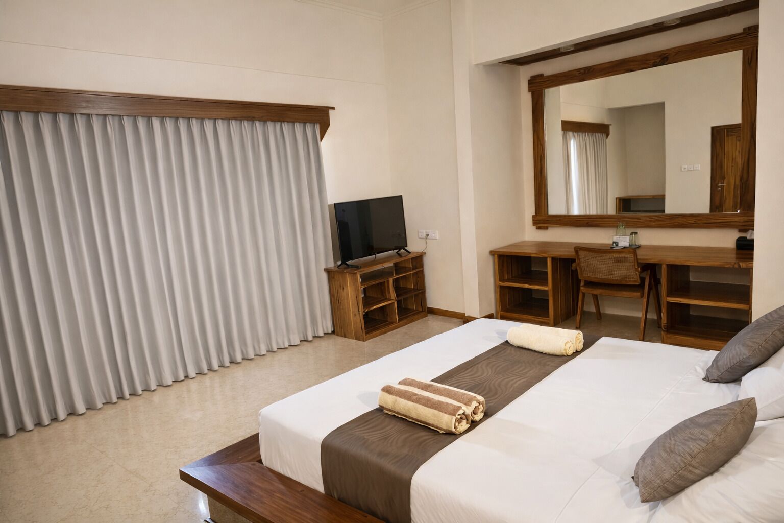 A hotel room with a bed, a desk, a television, and a large mirror.