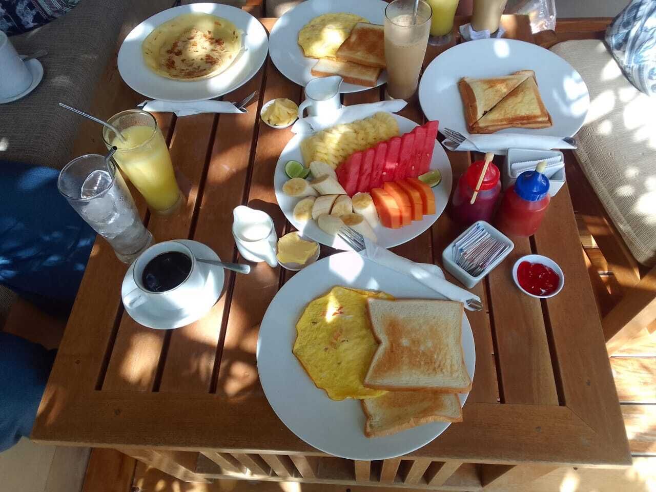 A wooden table with breakfast items including toast, eggs, fruit, and beverages.