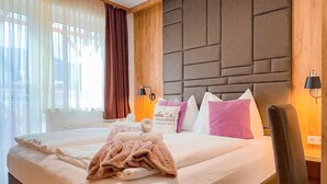 Una habitación de hotel con una cama grande, un cabecero de madera, un escritorio con silla y una ventana con cortinas.
