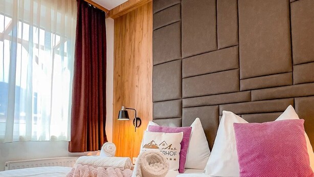 Habitación de hotel con una cama grande, un cabecero, una mesita de noche con lámpara y una ventana con cortinas.