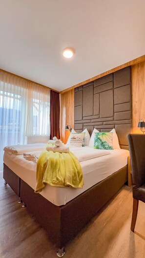 Hotelkamer met een groot bed, een hoofdbord met een geometrisch patroon, een houten accentmuur en een raam met dunne gordijnen.