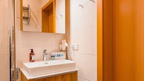 Ein Badezimmer mit einem Holzwaschtisch, einem weißen Waschbecken, einem Spiegel und einer Duschkabine.