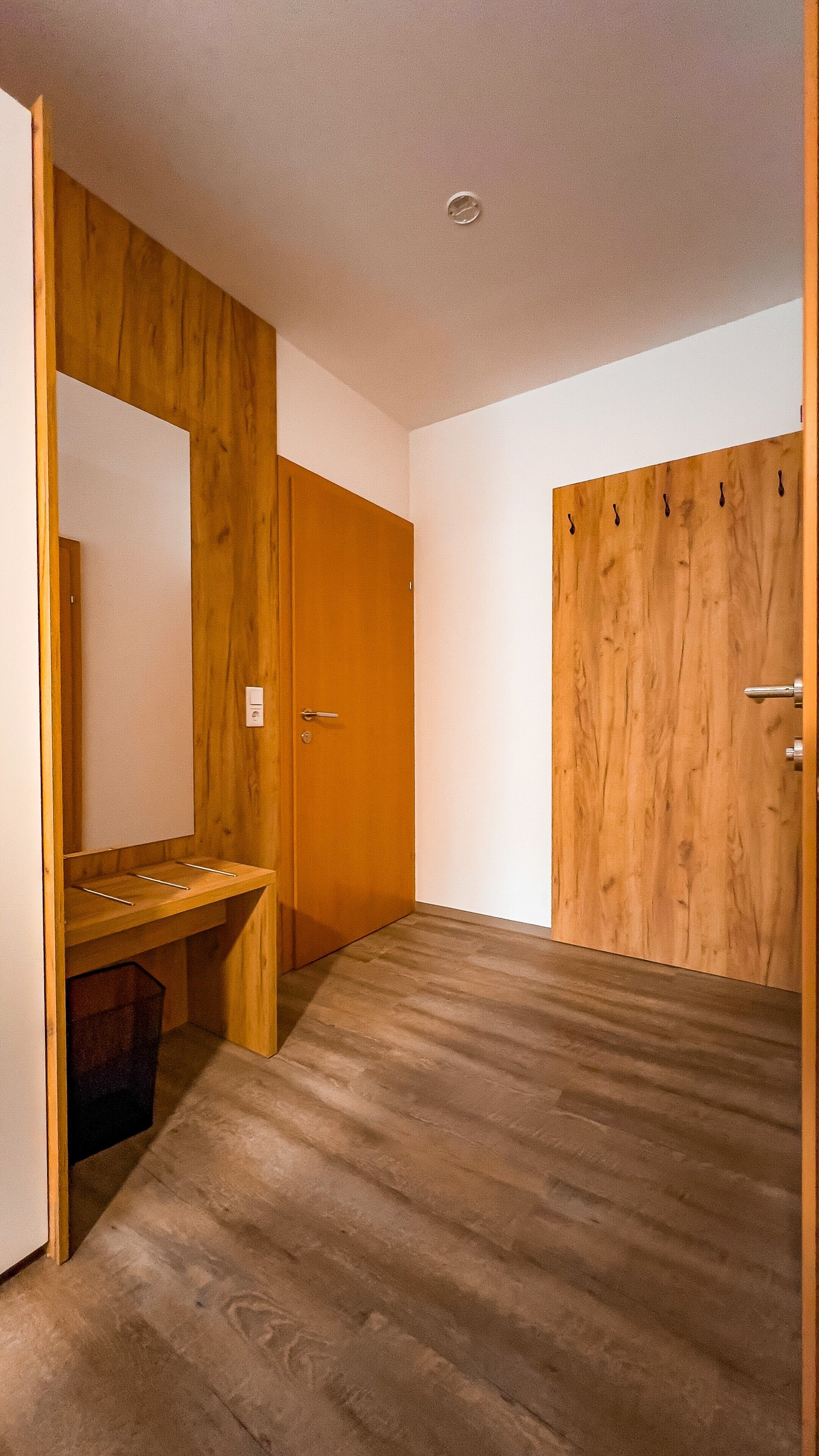 A room with a wooden wardrobe, a mirror, and a wooden desk with a chair.