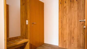 A room with a wooden wardrobe, a mirror, and a wooden desk with a chair.