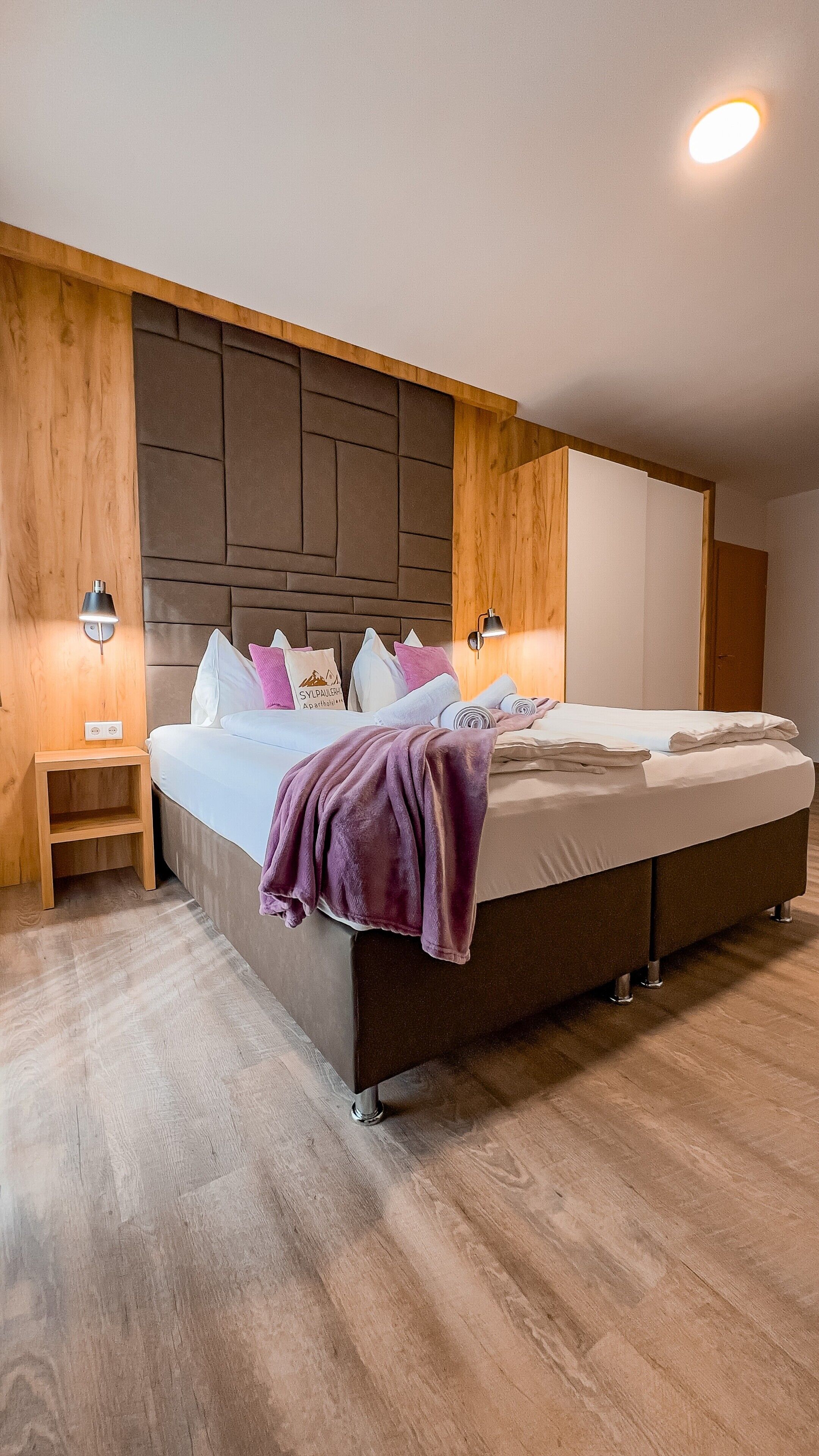 Ein modernes Schlafzimmer mit einem großen Bett, einem Holzkopfende, Nachttischlampen und Holzboden.