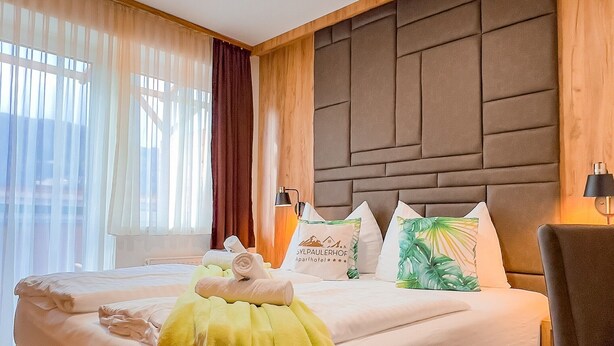 Ein Hotelzimmer mit einem großen Bett, einem Holzkopfstück, einem Stuhl und einem Fenster mit Vorhängen.