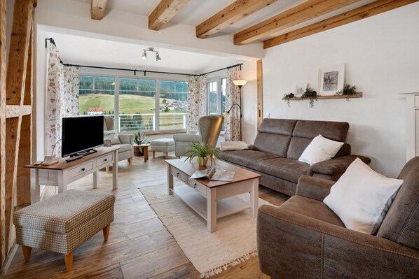 A living room with a sofa, TV, wooden coffee table, and a view of the outdoors. - Apartment 'Ferienwohnung Rinkenberg' with Private Terrace and Wi-Fi (Baiersbronn)