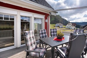 An outdoor patio with a table and chairs, a potted plant, and a view of houses and trees. - Apartment 'Ferienwohnung Rinkenberg' with Private Terrace and Wi-Fi (Baiersbronn)