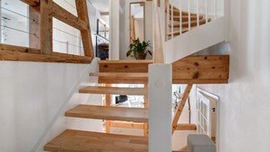 Un escalier en bois avec des rampes blanches, menant à un palier où se trouve un pot de fleurs.
