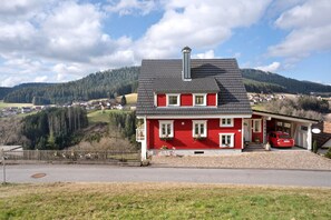 A red house with a grey roof, a chimney, and a small porch with a red car parked outside. - Apartment 'Ferienwohnung Rinkenberg' with Private Terrace and Wi-Fi (Baiersbronn)