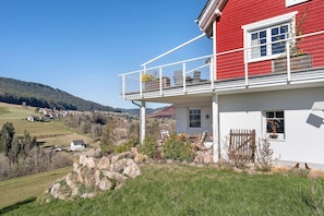 En röd byggnad med en balkong, en liten trädgård och utsikt över en by i bakgrunden.