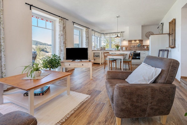 Ett vardagsrum med en tv, en soffa, ett matbord och ett kök i bakgrunden.