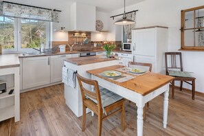 Una cocina moderna con mostradores de madera, una isla central y un comedor con mesa y sillas de madera.