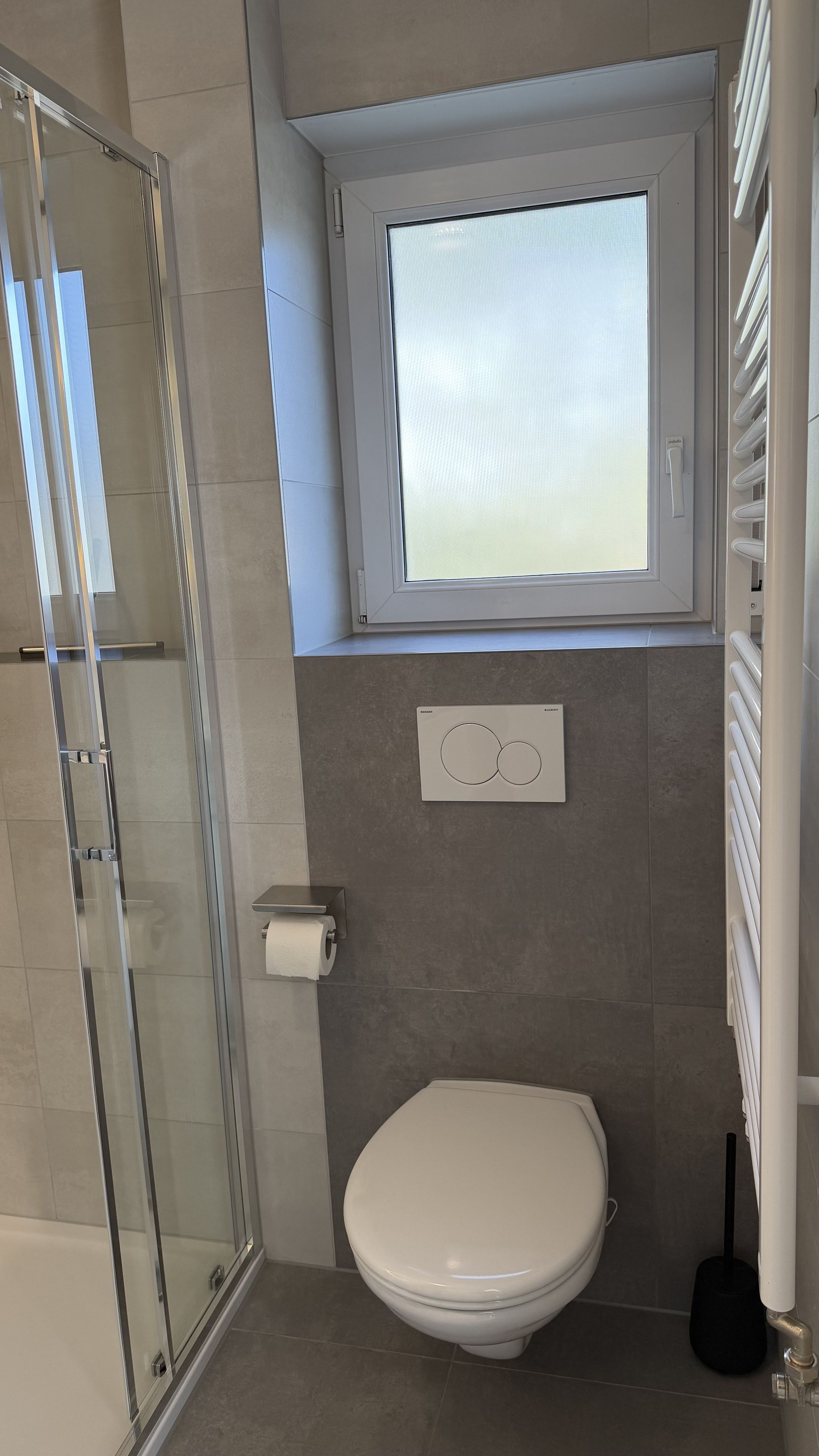 A bathroom with a toilet, a glass shower enclosure, and a window above the toilet.