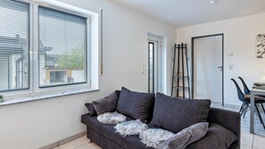 Un salon moderne comprenant un canapé, une table à manger avec des chaises, un porte-manteau et une fenêtre avec des stores.