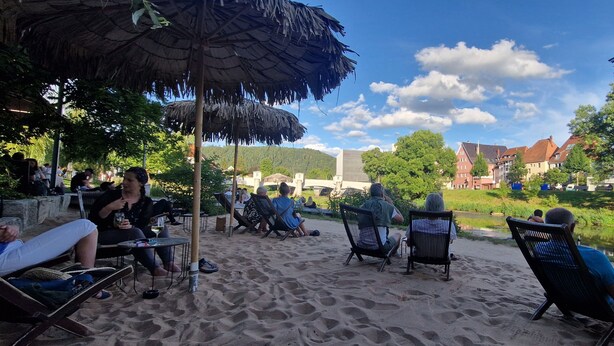 A beachside setting with lounge chairs, umbrellas, and a calm water body.