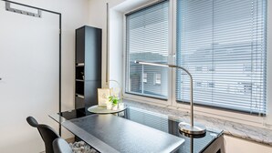A modern room with a glass table, a chair, a desk, a radiator, and a window with blinds.