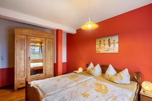 Une chambre avec une armoire en bois, un lit avec une literie à motifs floraux, un tableau au mur et un luminaire suspendu.