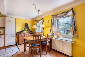 Une cuisine avec des meubles en bois, une table à manger, un radiateur et une fenêtre avec des rideaux.