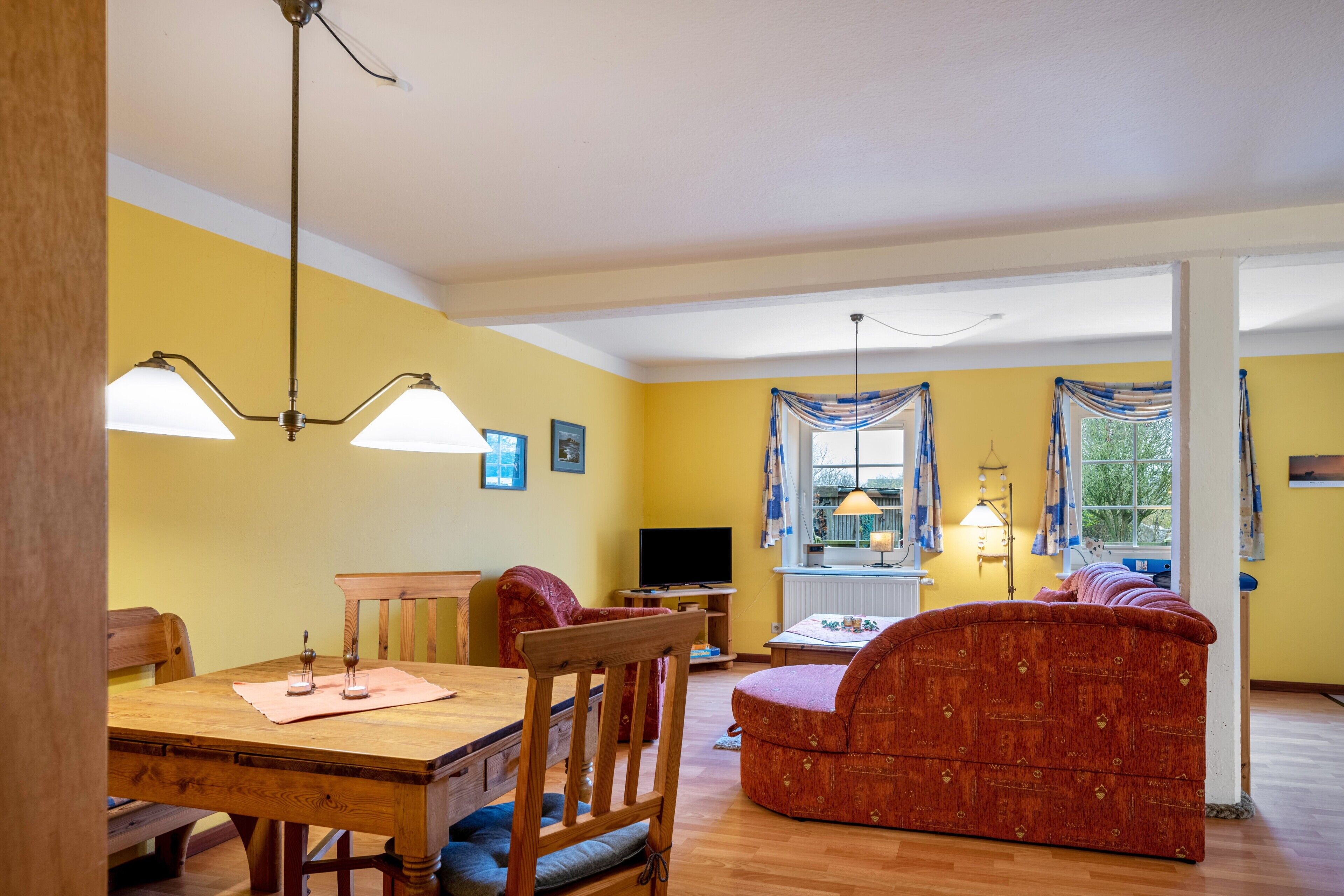 Un salon avec une table à manger en bois, un canapé rouge, un téléviseur et une fenêtre avec des rideaux.