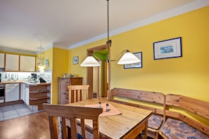 Cozinha com armários de madeira, mesa de jantar com cadeiras, um banco e uma luminária pendente.
