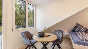 Ein modernes Schlafzimmer im Loft-Stil mit großem Fenster, einem runden Holztisch, zwei Stühlen, einer Couch und einem Nachttisch mit Lampe.