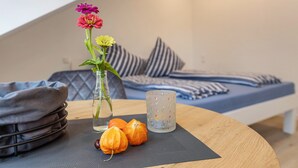 Ein ordentlich eingerichteter Raum mit einem Bett, Kissen, einer Vase mit Blumen und einer Kerze auf einem Tisch.
