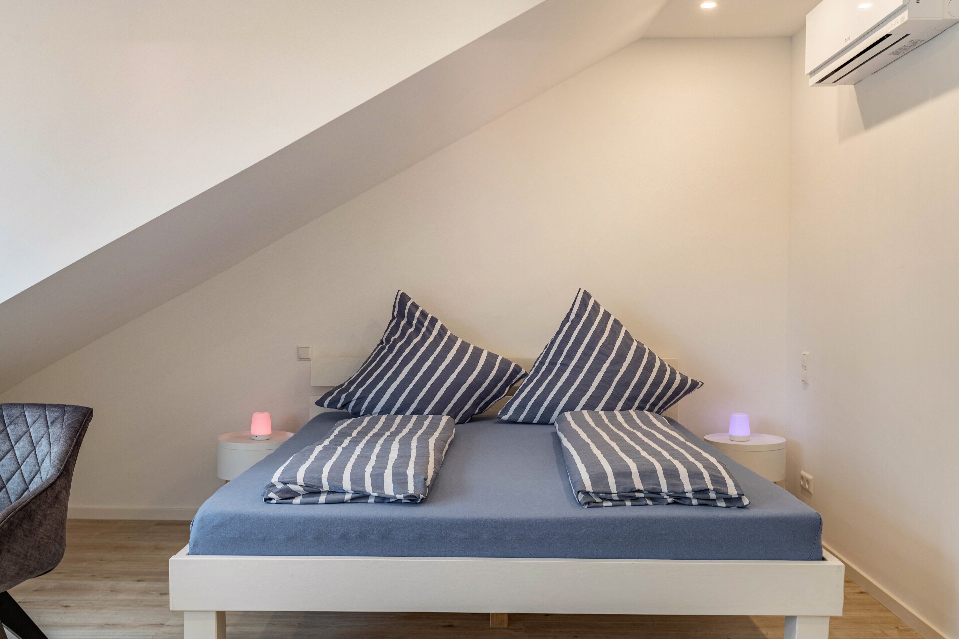 A bedroom with a bed, pillows, bedside tables, and an air conditioning unit.