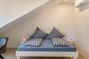 A bedroom with a bed, pillows, bedside tables, and an air conditioning unit.