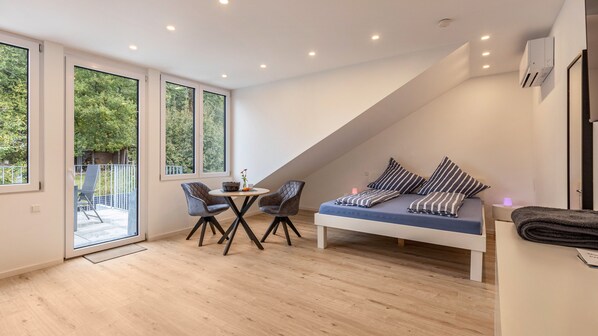 A modern loft bedroom with a large window, a dining area, and a built-in bed with striped pillows.