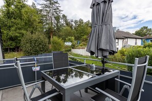An outdoor patio with a glass table, metal chairs, and a grey umbrella.