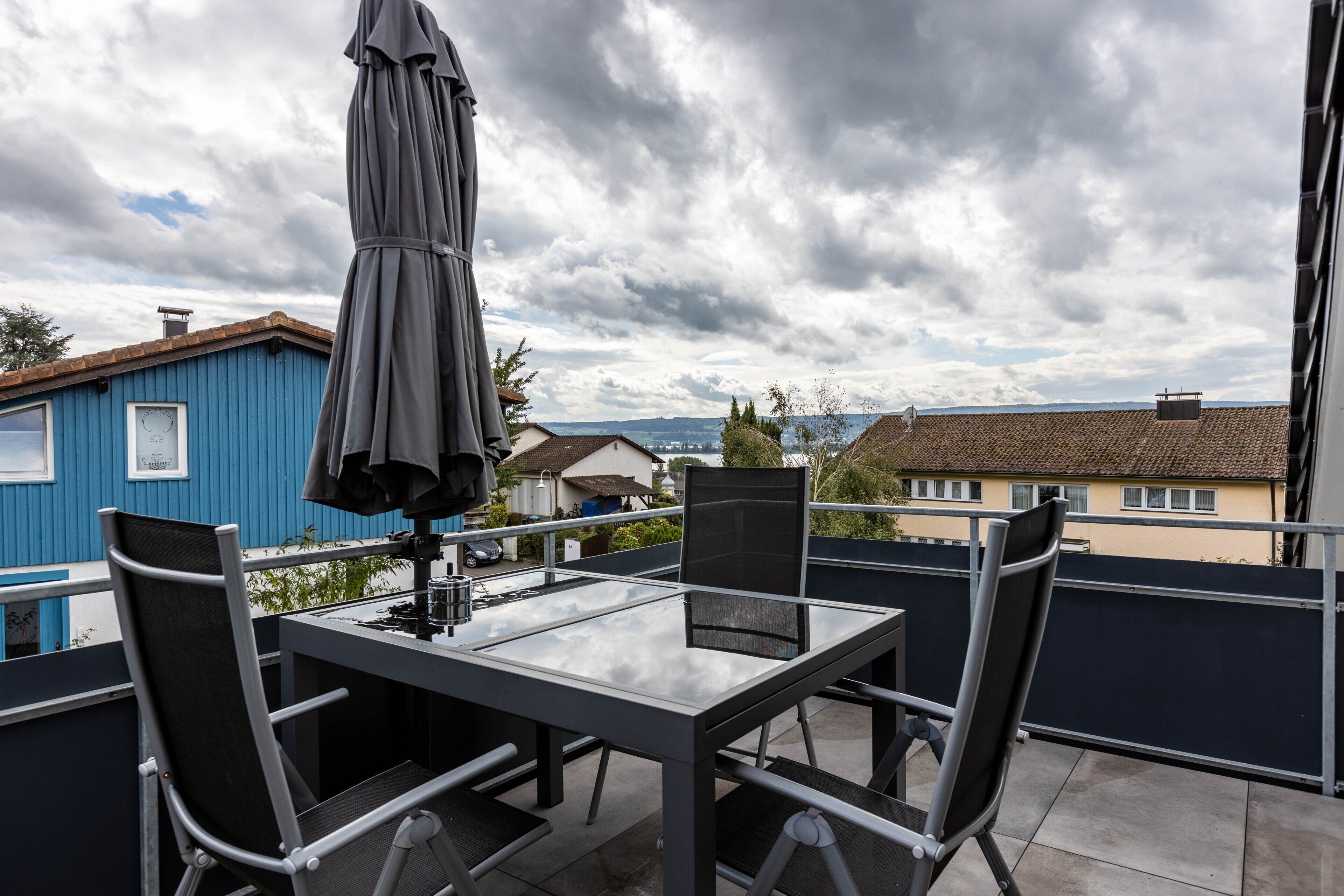 Un balcon avec une table et des chaises, un parasol et une vue sur des maisons et une étendue d’eau.