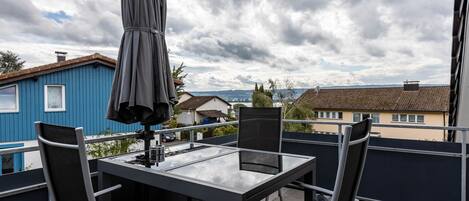 Un balcon avec une table et des chaises, un parasol et une vue sur des maisons et une étendue d’eau.