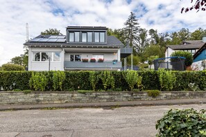 A modern two-story house with a balcony, solar panels, and a stone wall.