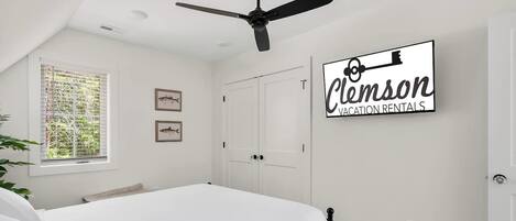 Una camera da letto con un letto, una ventola a soffitto, una finestra con persiane e un cartello a parete.