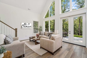 A spacious living room with a large window, a staircase, and a sign for Clemson Vacation Rentals.