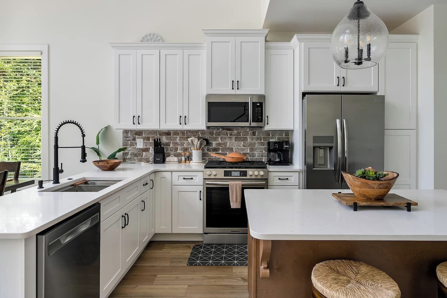 Una cucina moderna con mobili bianchi, un forno a microonde, un fornello, un frigorifero e un lampadario.