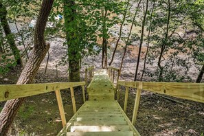 A wooden bridge leading into a forested area with trees and a dirt path.
