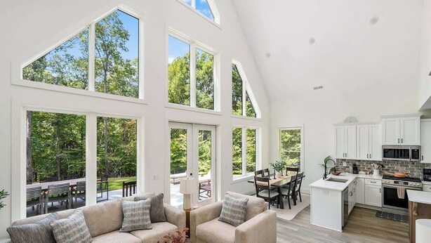 A spacious living area with a large sofa, a dining table, and a kitchen with white cabinets and a stone backsplash. - Clemson Cove - Beautiful new construction on outskirts of Clemson! (Central)