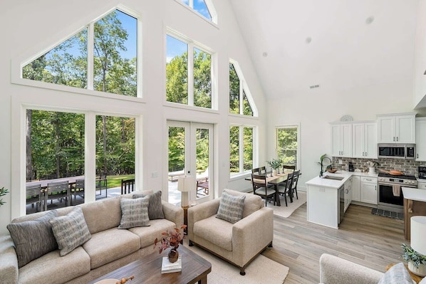 A spacious living area with a large sofa, a dining table, and a kitchen with white cabinets and a stone backsplash.
