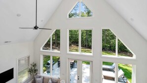 A high-ceilinged room with a sloped roof, large windows, and a ceiling fan. - Clemson Cove - Beautiful new construction on outskirts of Clemson! (Central)