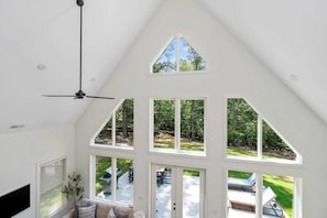 A high-ceilinged room with a sloped roof, large windows, and a ceiling fan.
