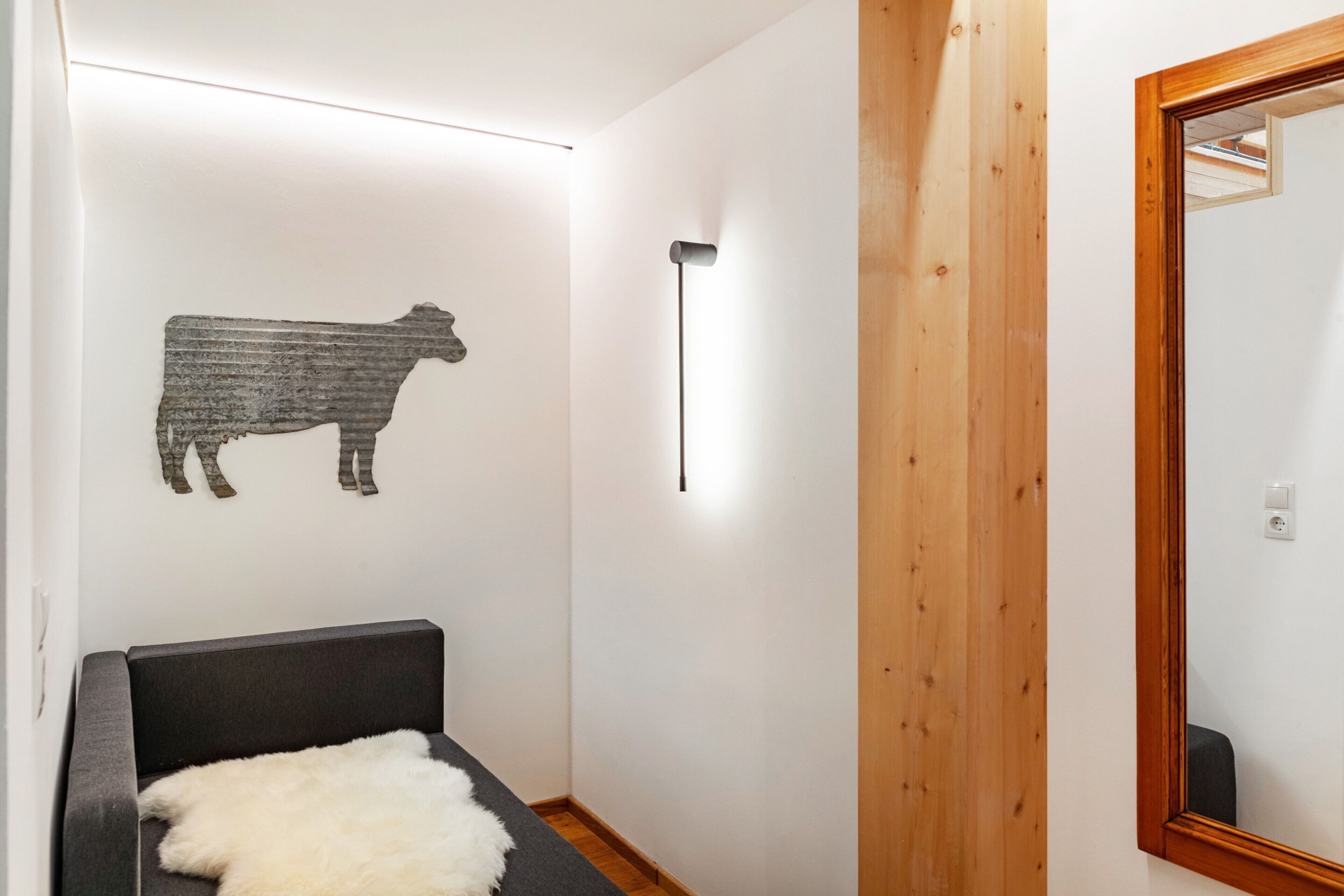 Et værelse med en sofa, en vægmonteret lampe og et spejl med træramme.