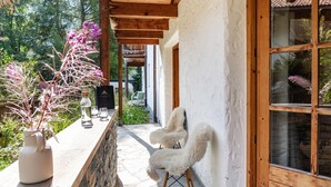 Una pérgola de madera, una pared blanca, un ventanal grande y una silla blanca.