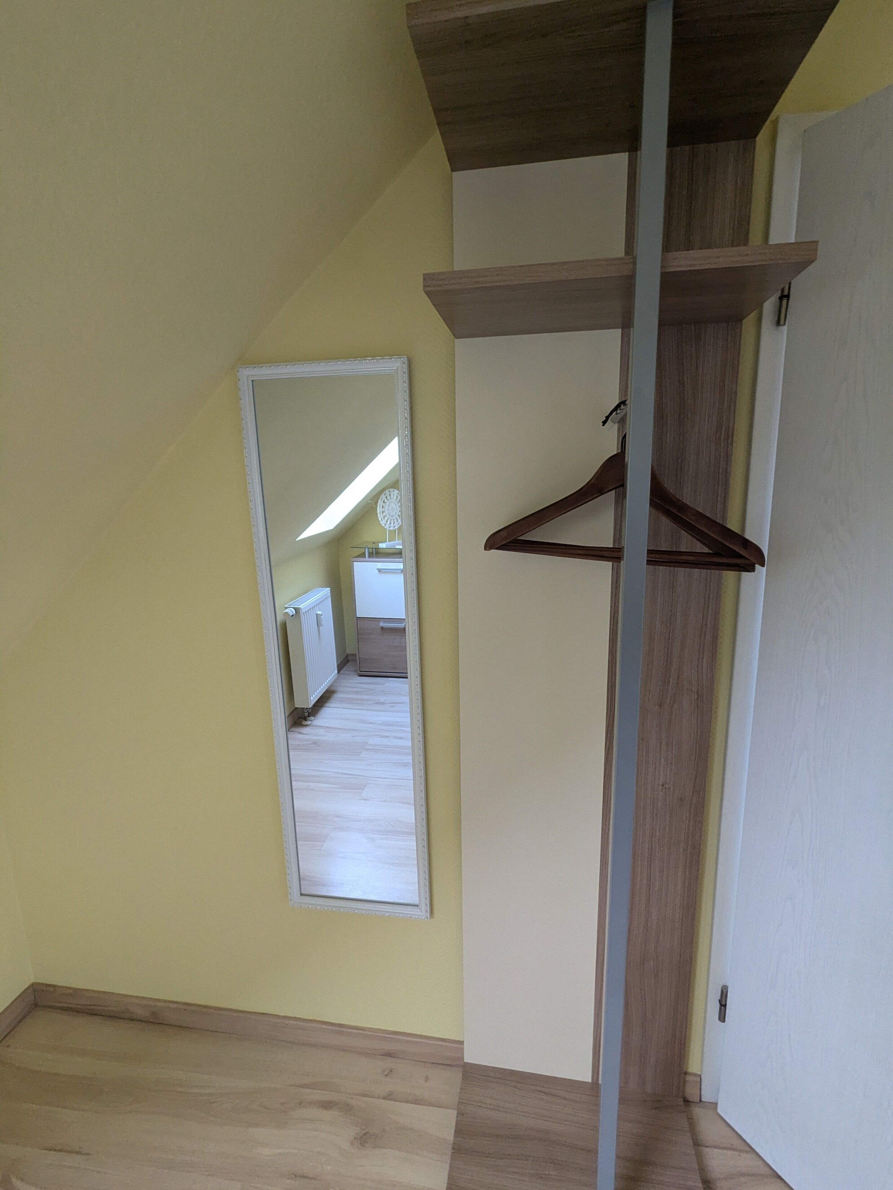 A room with a wooden floor, a white door, and a mirror on the wall.