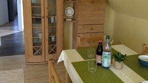 A dining area with a table set for two, a wooden cabinet with glass doors, and a plant on the wall.