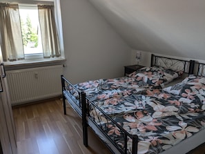 A bedroom with a bed, a window with curtains, a radiator, and a nightstand.