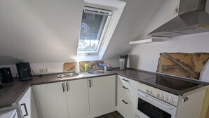 A compact kitchen with white cabinets, a built-in stove, a window, and a stone backsplash.